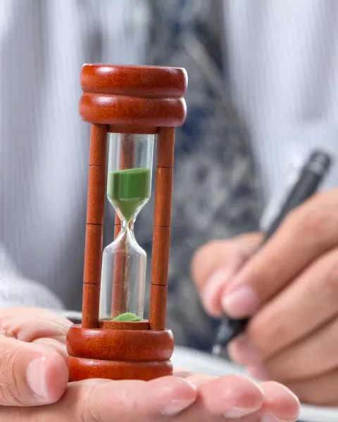 hourglass in white collar worker man's hand, with pen in the other