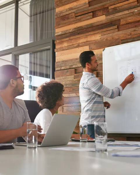 Male office worker giving training session to his colleagues using a whiteboard.