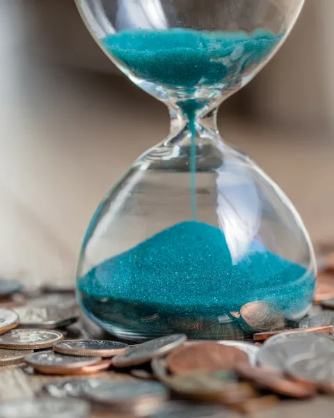 Time is money concept with an hourglass surrounded by coins.
