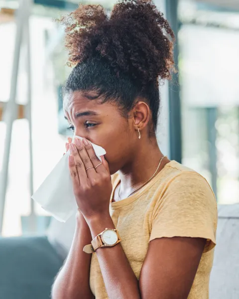 Shot of a young woman feeling ill and blowing her nose sitting on the sofa at home.