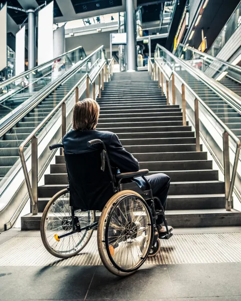 Businessman in a wheelchair facing stairs and escalators.