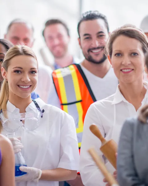 A multi-ethnic group of varied business professionals are standing tgoether and are smiling while looking at the camera.