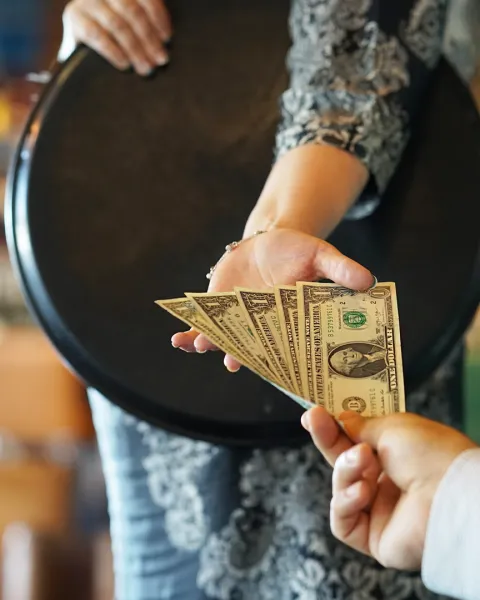 The hand of the waitress, holding a tray, takes tip money being handed to her.
