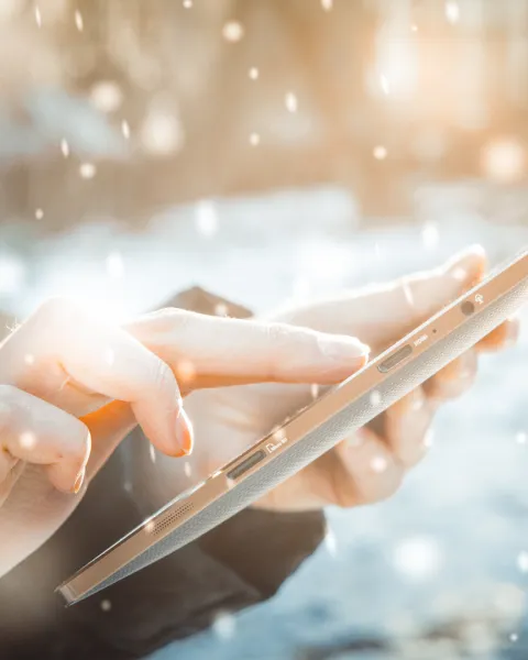Close-Up of a man's hands holding up and looking at a tablet in a snowstorm.