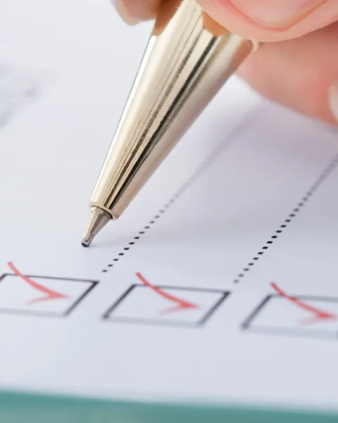 Close-up of a hand holding a pen checking off boxes on paper.