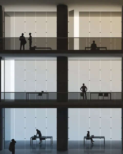 Backlit office workers in their cubicles in an office building of several floors.
