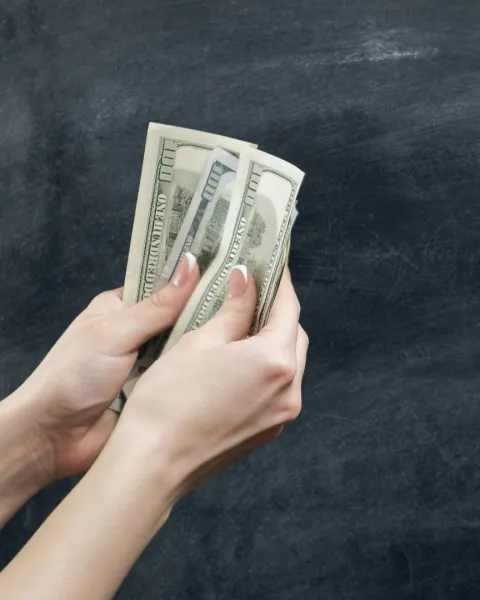 Close-up of two hands. One hand holding dollar bills and the other hand is open/outstreched asking for money.
