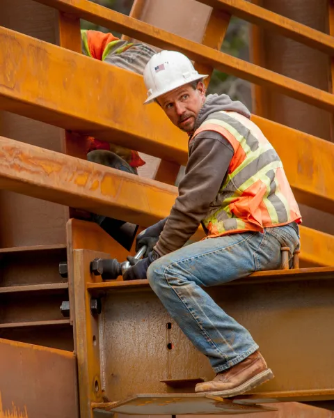Construction worker sitting on a beam while working on a bridge construction job.