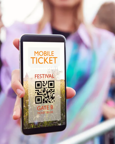 Close-up of woman holding a mobile phone screen to camera as she arrives at entrance to music festival.