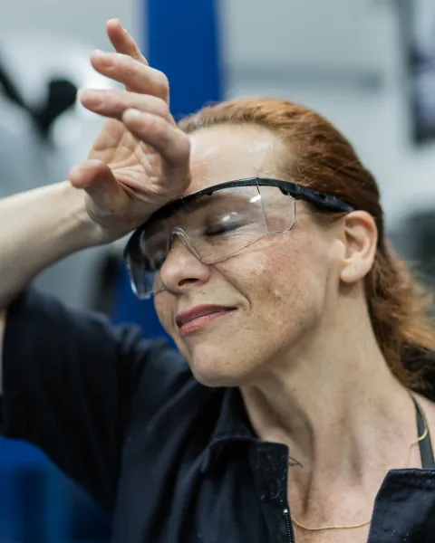 Close up of a tired and hot female factory worker wiping sweat from her forehead.