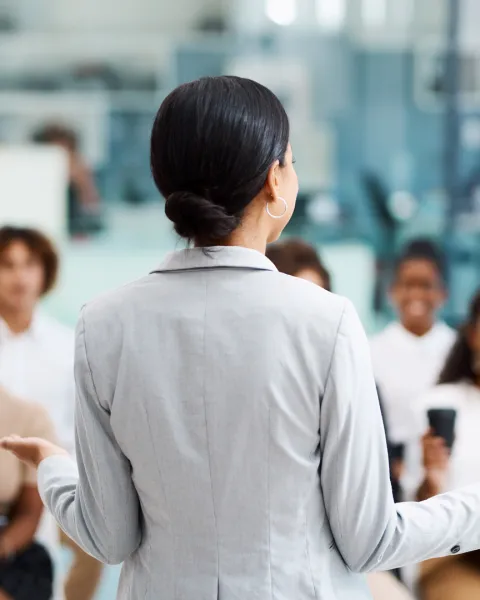A view from behind a woman presenting to, or training, a team of employees.