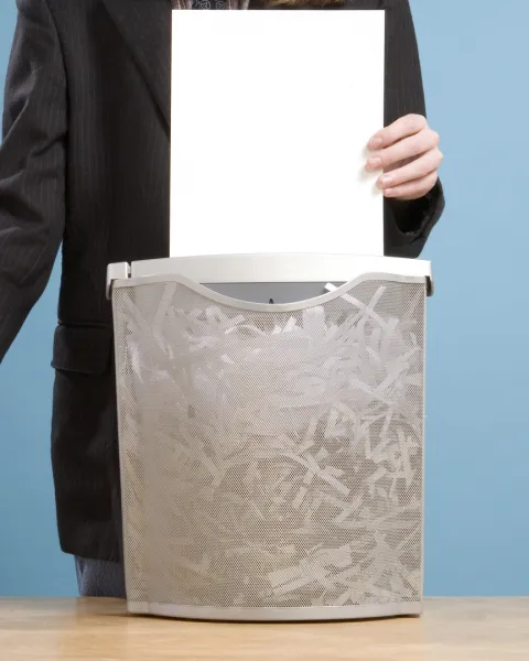 Close-up of a man feeding paperwork from a large pile into a shredder.