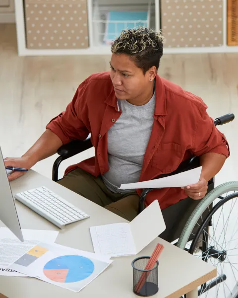 A businesswoman in a wheelchair at a desk working from a home office.