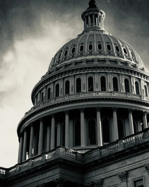 Monochromatic image of a darkened US Capitol building in front of a dark and stormy sky.
