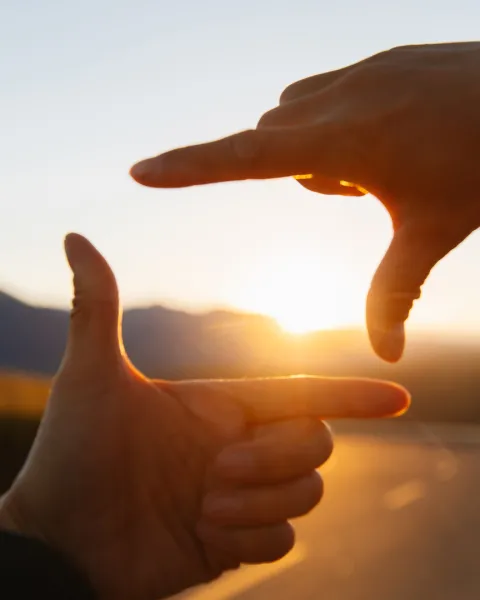 Two hands forming a picture frame with the sunset within the frame.