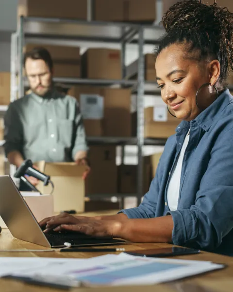 Diverse female and male warehouse inventory managers talking, using laptop computer and checking stock.
