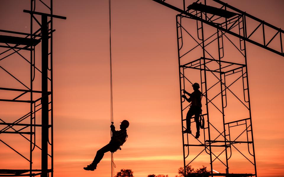 Two construction workers on scaffolding at dusk.
