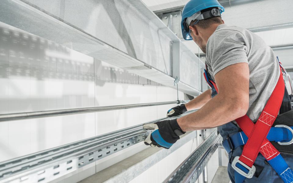 Construction worker wearing hardhat, harness, safety gloves.