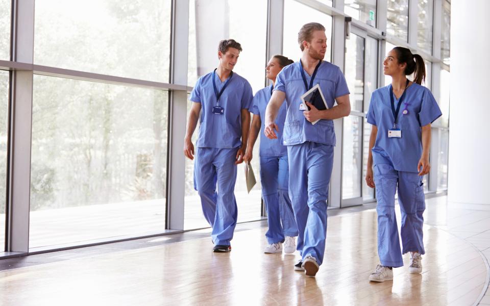 Team of healthcare workers in scrubs walking down hallway.