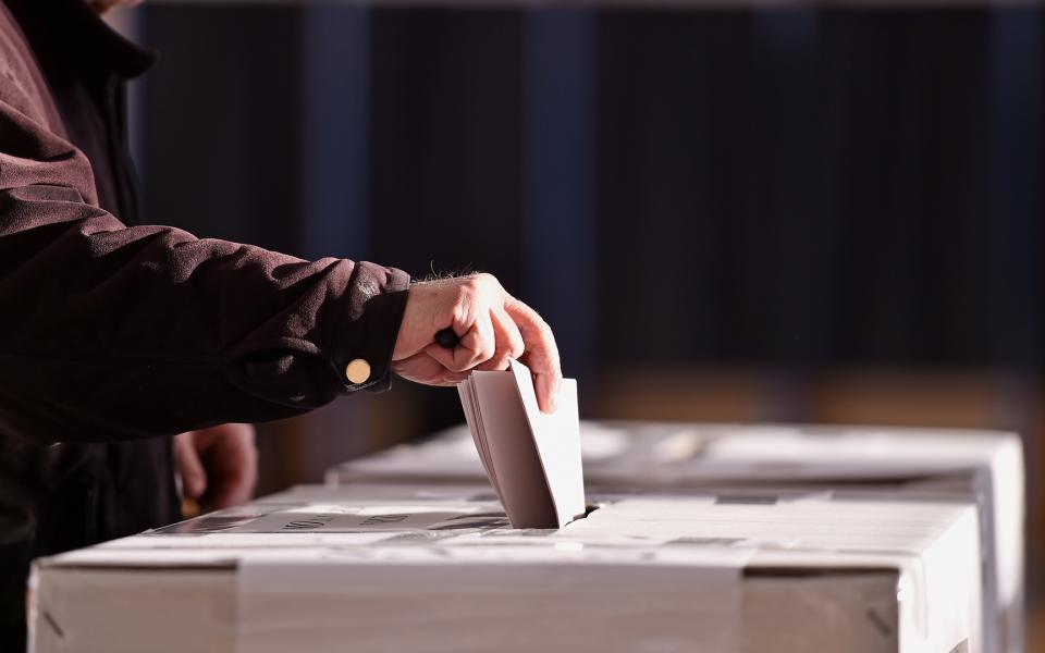 Hand placing their vote into a ballot box.