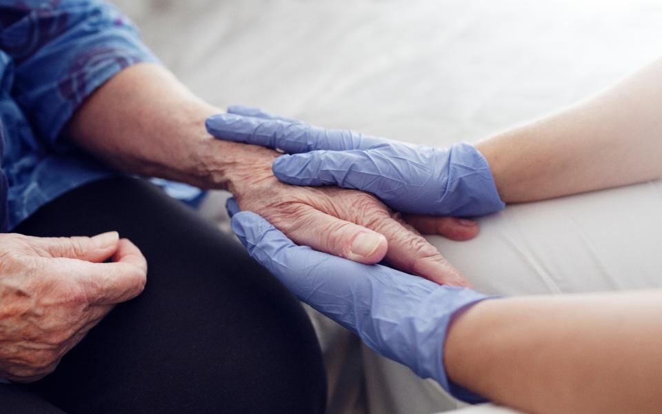 A pair of hands in surgical gloves comfort the hands of an elderly person.