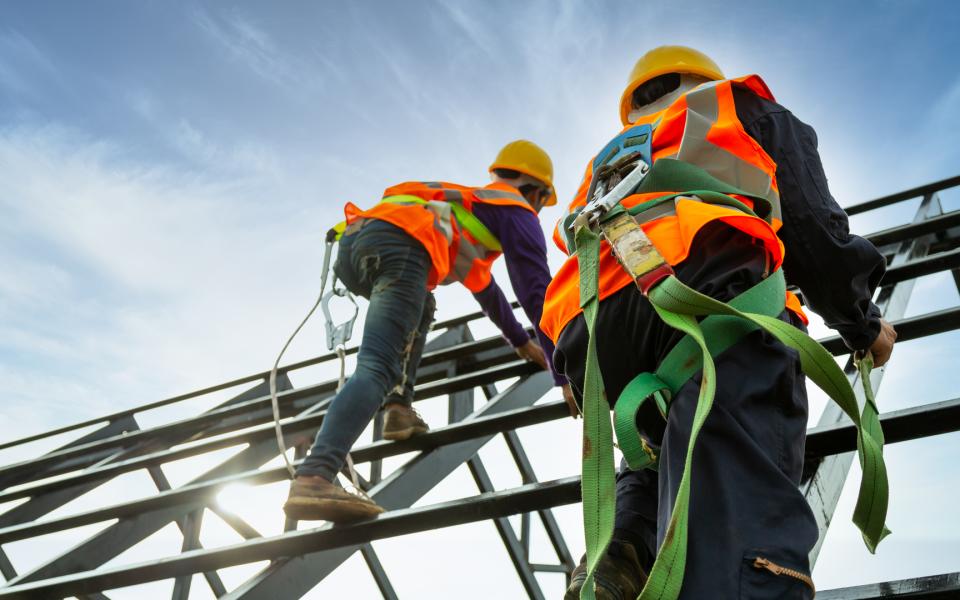 Two construction workers wearing safety vests and harnesses.