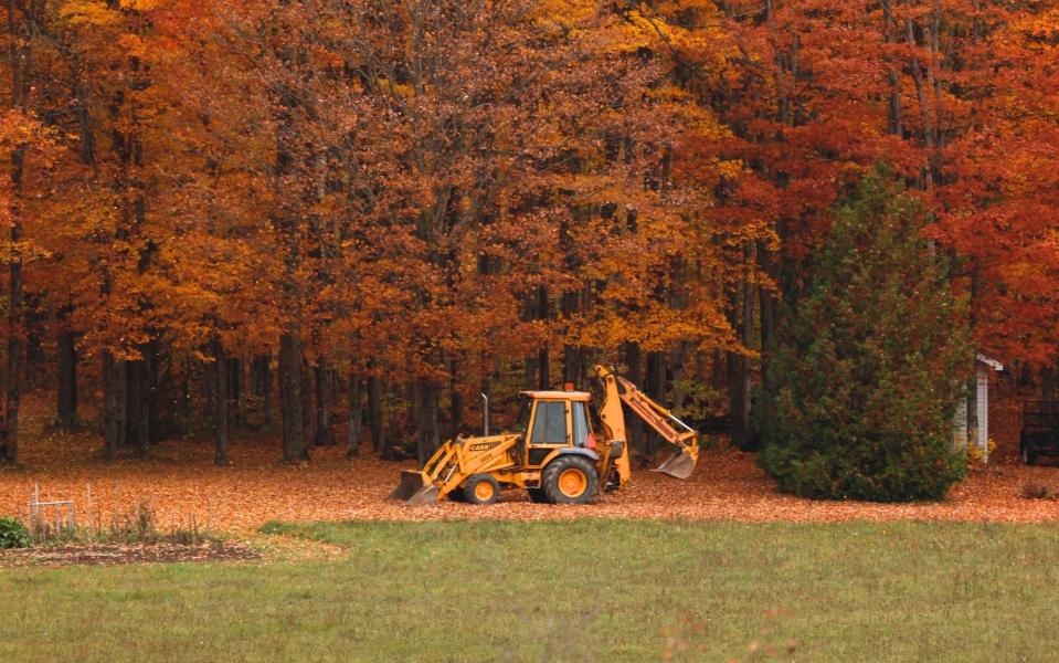 A single back hoe with a backdrop of trees in Fall colors.