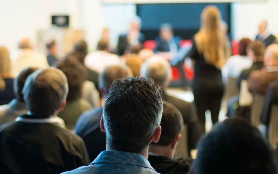 A town hall type meeting with a woman posing a question to a panel.