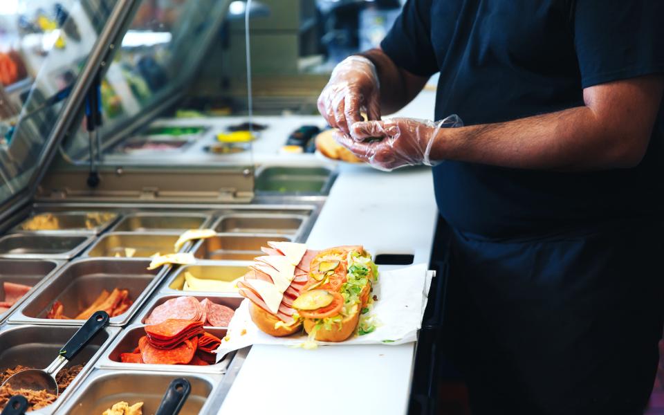 Image of a man's hands creating a sandwich at a fast food restaurant.