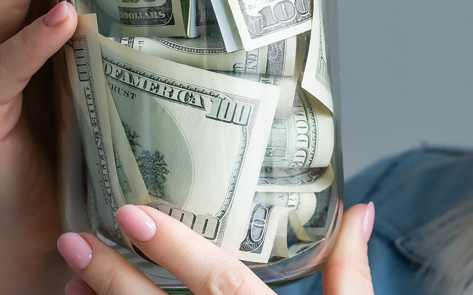 A woman's hands holding a clear jar full of money.