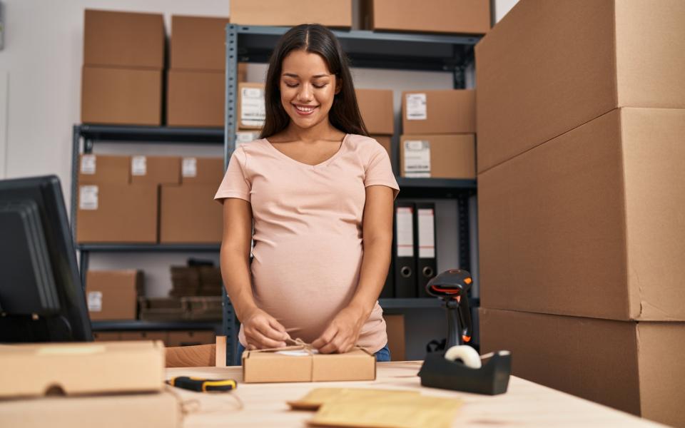 A pregnant woman at work in a warehouse labeling cartons.