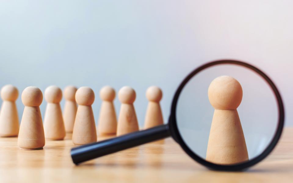 A magnifying glass getting a close-up look at one wooden figure in a row of many wooden figures.