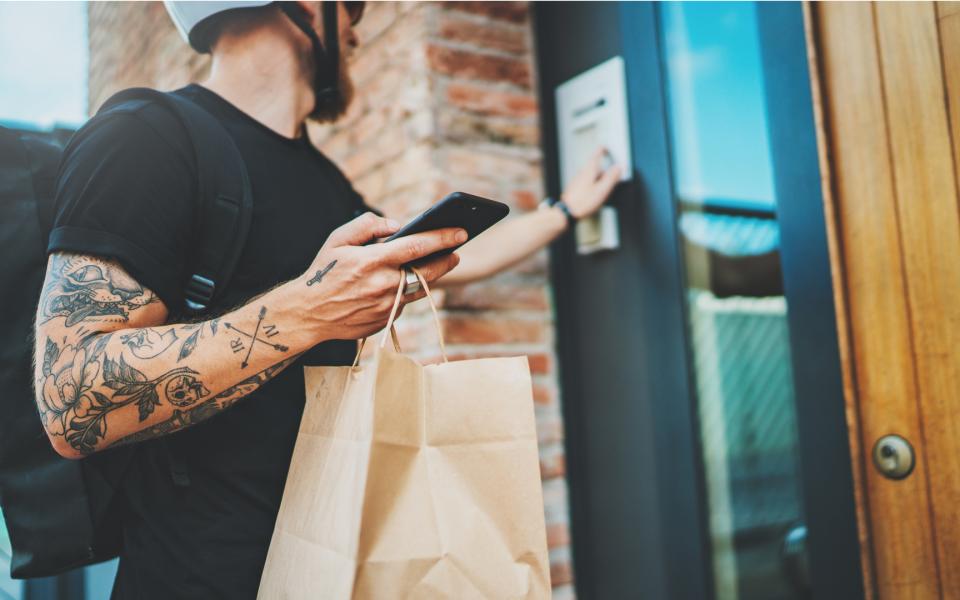 A food delivery person ringing the door bell with bag and smartphone in hand.