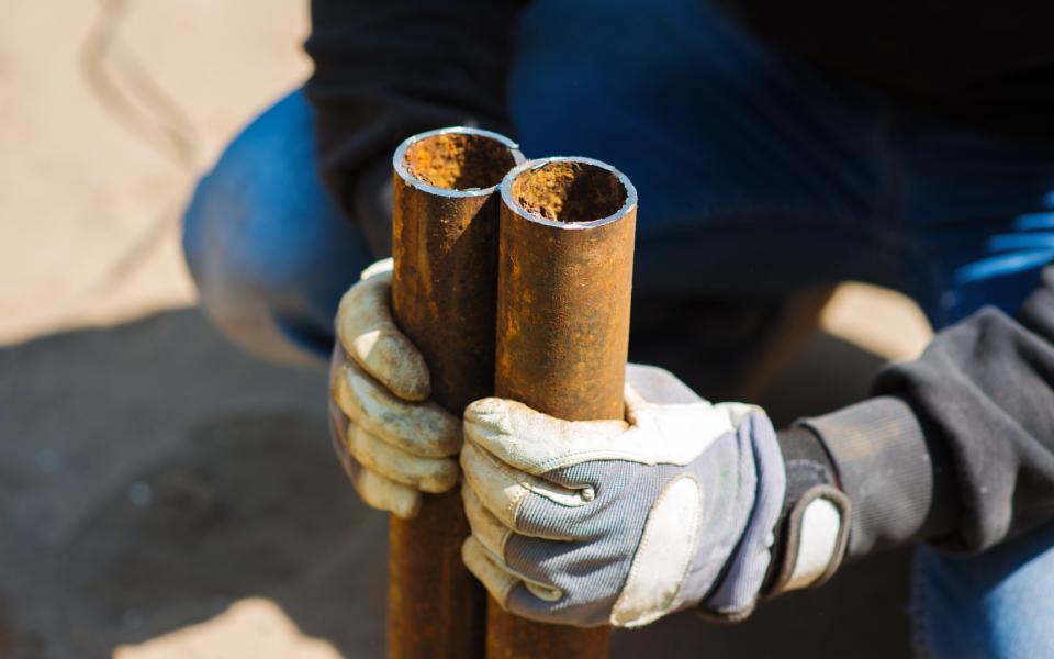 A worker holds two pieces of a cut metal pipe in his gloved hands.