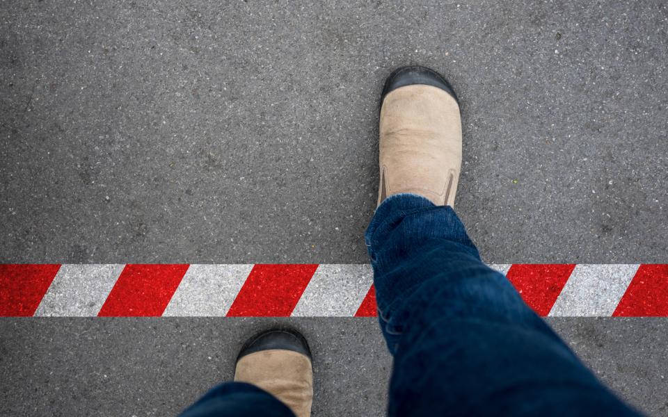 Looking down at shoes walking across red and white line to prohibited area.