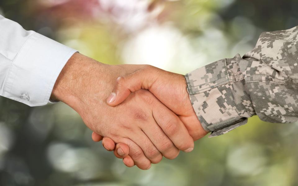 Close-up of two hands shaking: one wearing a business shirt and one wearing a military uniform.