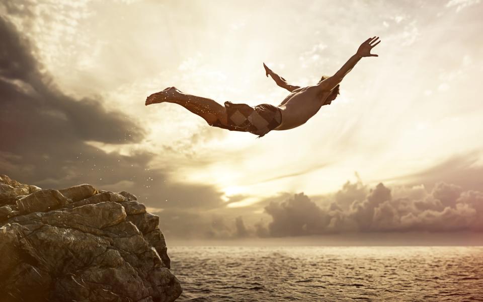 A man diving off a cliff into the ocean.