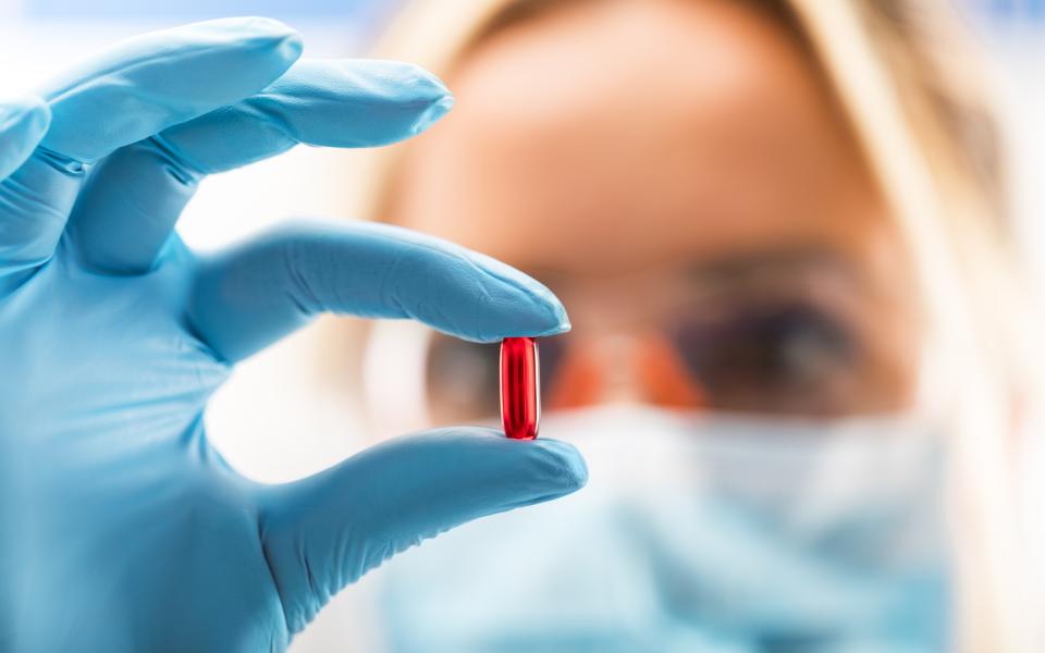 Close-up of a doctor looking at her gloved hand holding up a red capsule.