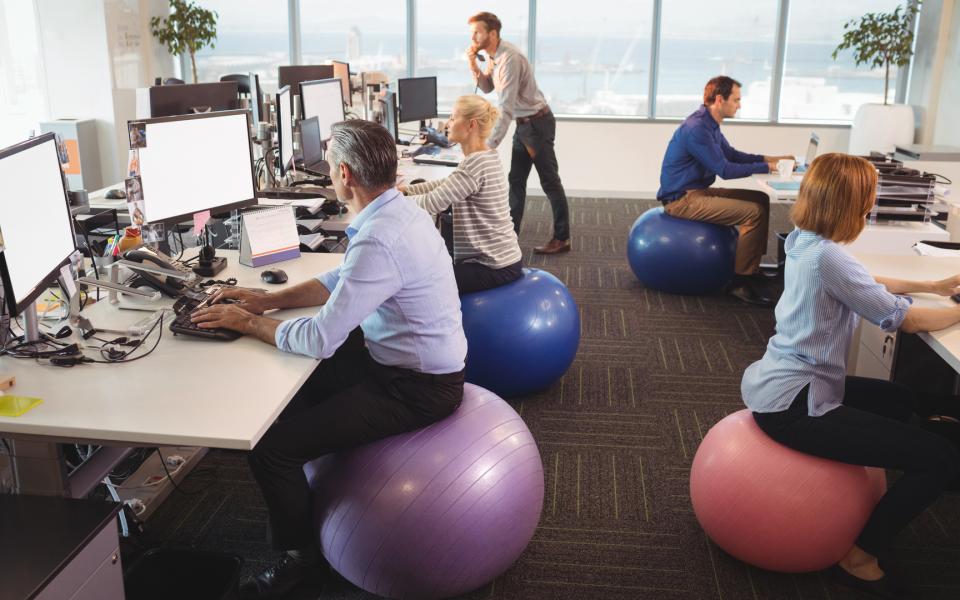 An office with employees sitting on exercise balls at their desks.