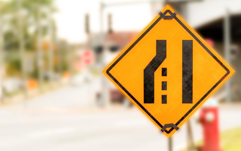 A black on yellow Left Lane Ending road sign.