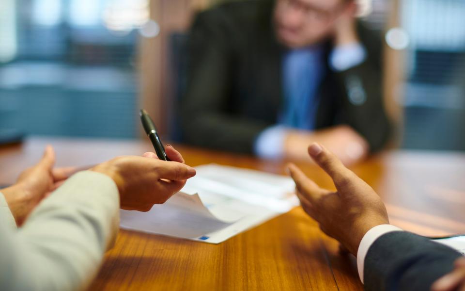 A dejected man at the end of a conference table and the hands of two people reprimanding him.