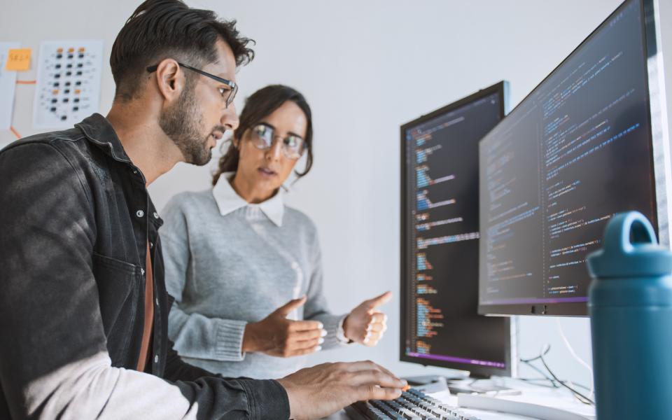 A male and female software developers discussing project in front of computers.