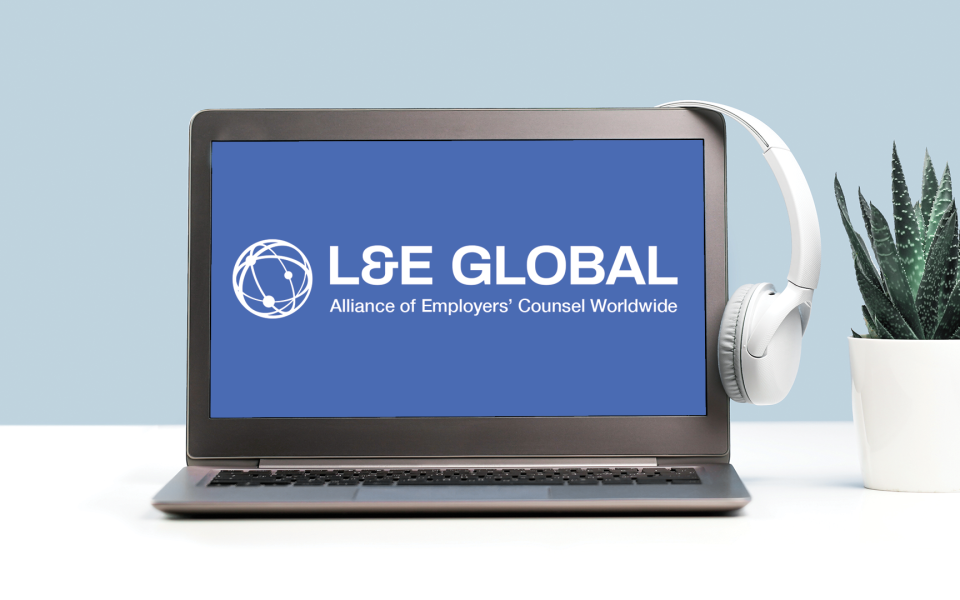 A laptop with headphones hanging on it with the L&E Global logo on the screen.