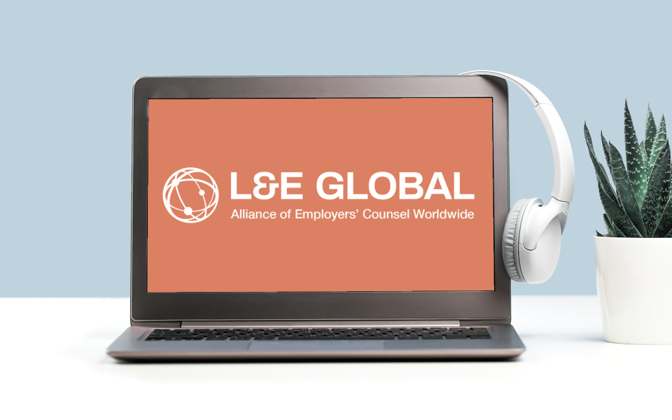 A laptop with headphones hanging on it with the L&E Global logo on the screen.