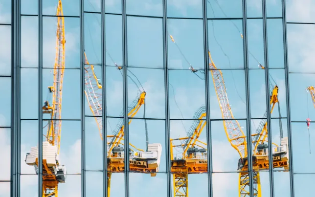 Construction cranes reflected in the exterior of a glass building