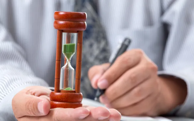 hourglass in white collar worker man's hand, with pen in the other