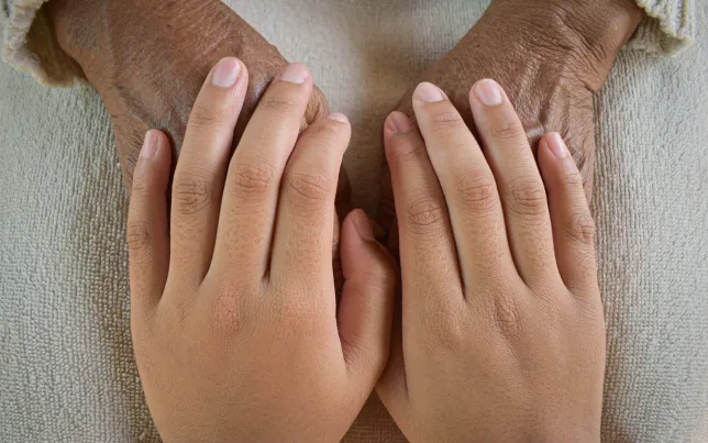 A pair of young hands comforting a pair of older hands.