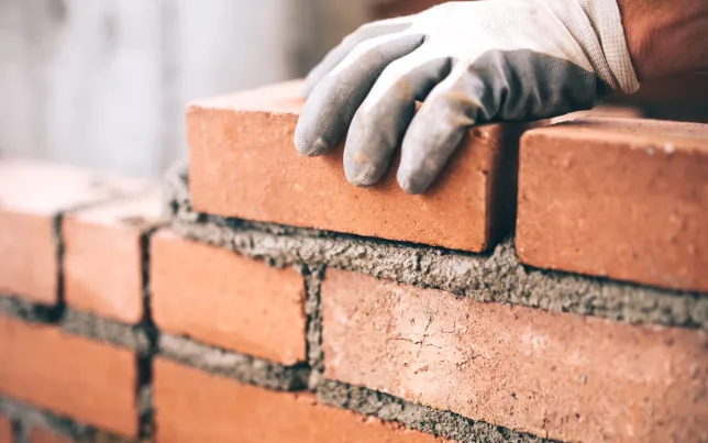 A close-up of a gloved hand laying bricks.