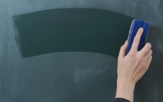 A hand with an erasure wiping a chalkboard clean.
