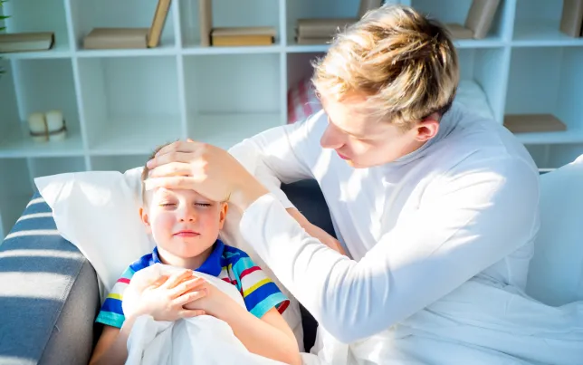 A father comforting his sick son by feeling his forehead.